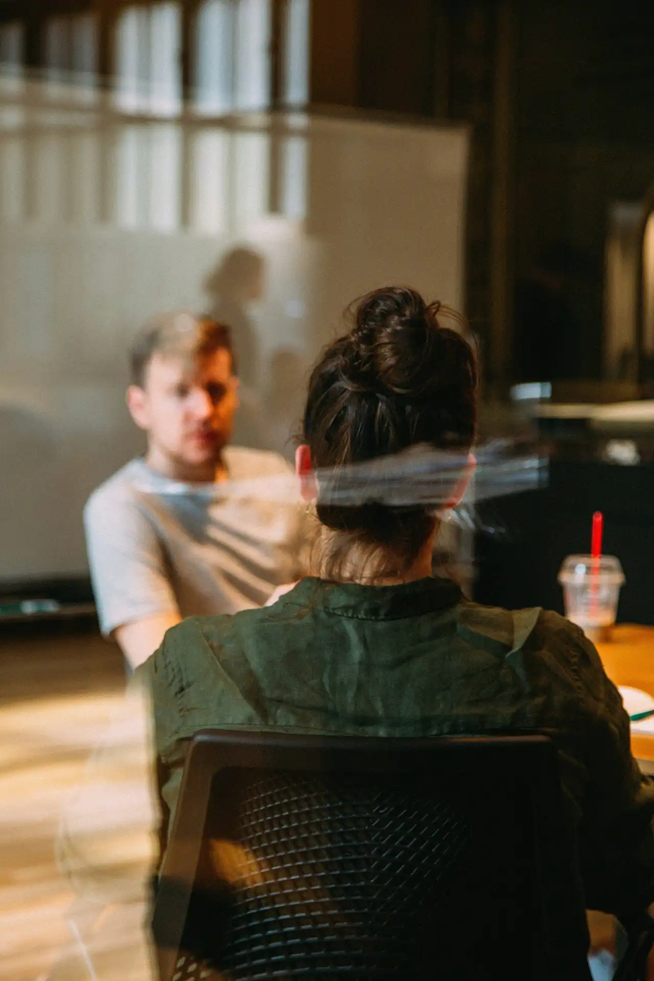 A back shot of a woman sitting in a conference room, listening to others sitting down at a table.