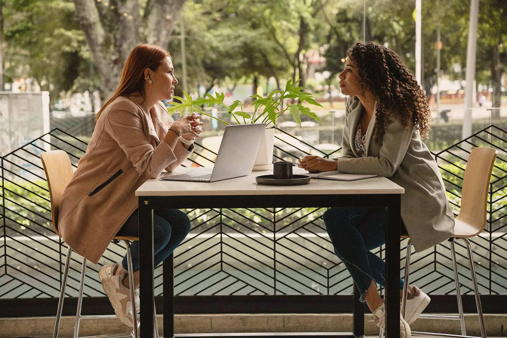 2 women sitting at a table outside, drinking coffee and chatting about business development. 